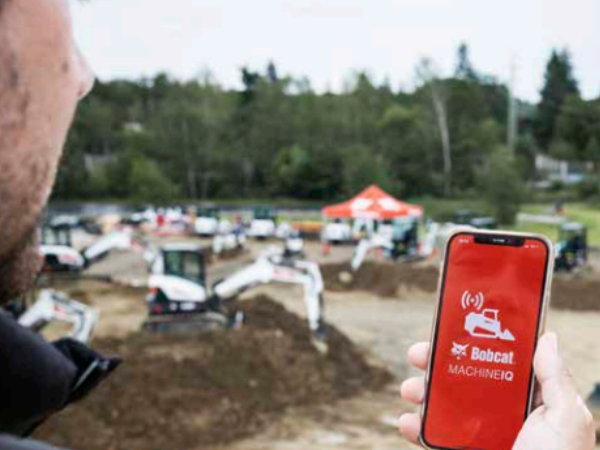 Nutzer mit Smartphone und Machine IQ-App vor einem Bobcat-Maschinenpark
